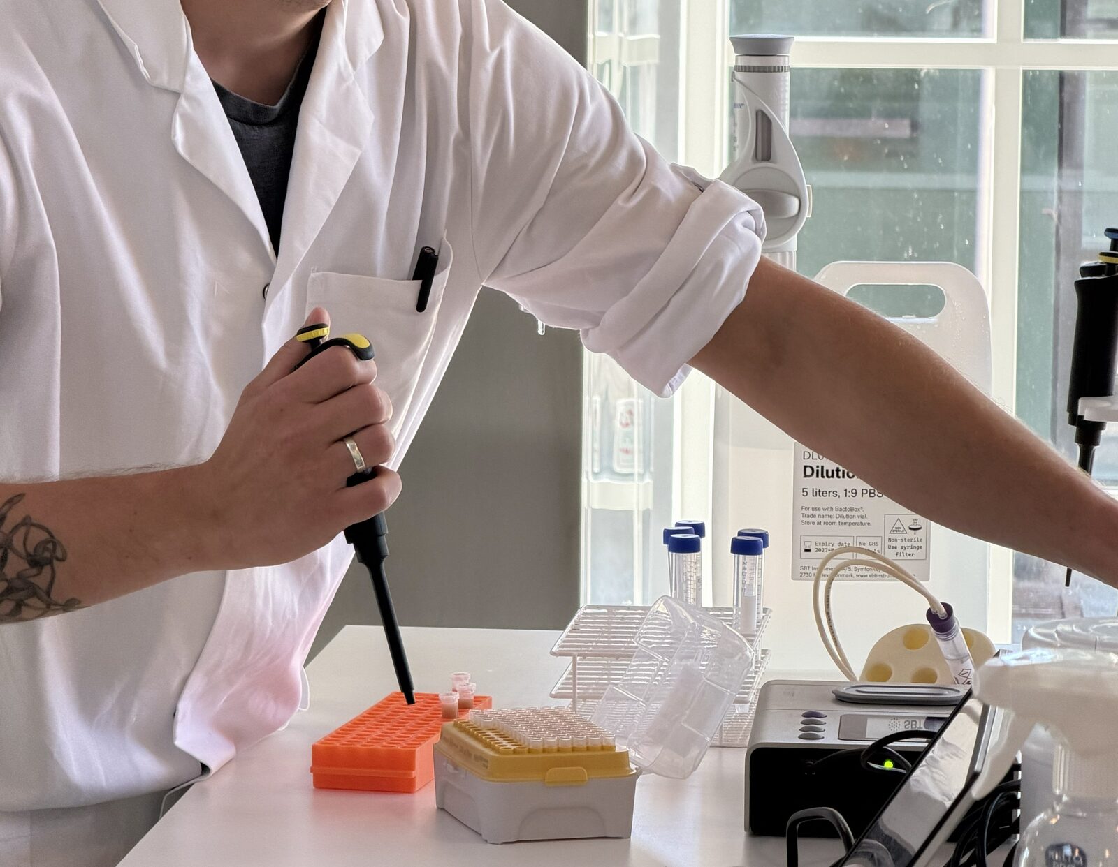 A scientist pipetting a sample into a tube next to a BactoBox at the lab bench
